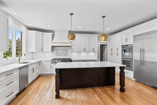 kitchen featuring a kitchen island, appliances with stainless steel finishes, pendant lighting, sink, and custom range hood