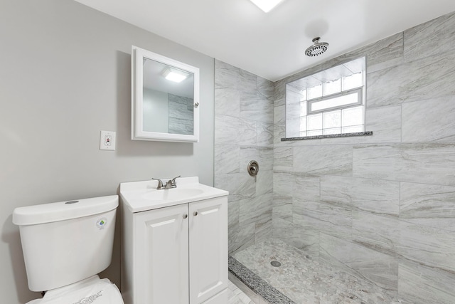 bathroom with tiled shower, vanity, and toilet