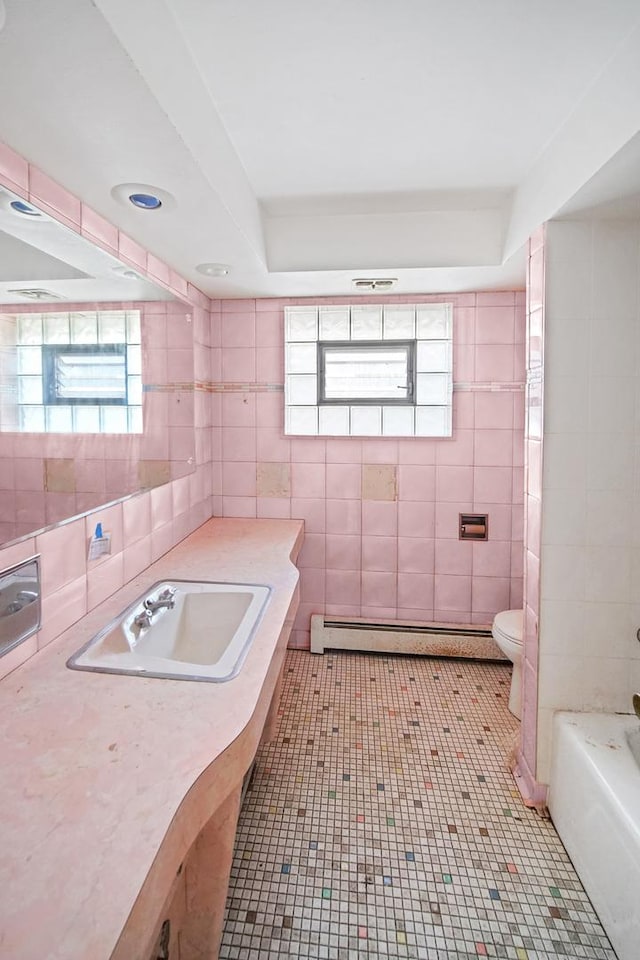 bathroom with a bath, a baseboard heating unit, tile patterned floors, toilet, and tile walls