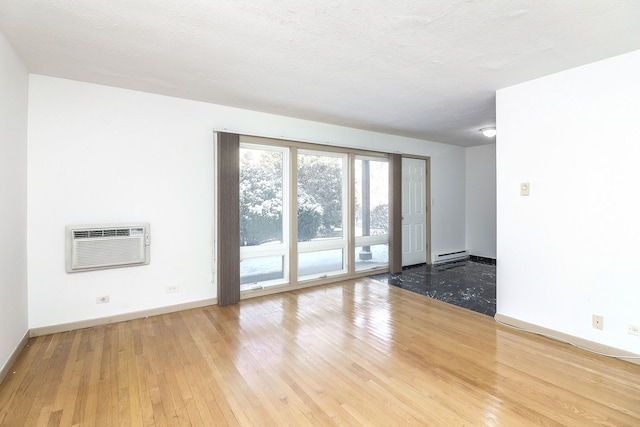 spare room featuring a wall mounted AC, wood-type flooring, a textured ceiling, and baseboard heating