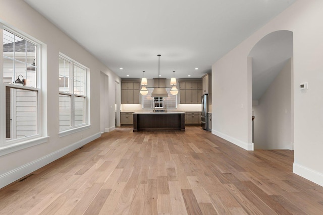 kitchen with stainless steel fridge, light wood-type flooring, decorative light fixtures, and a kitchen island