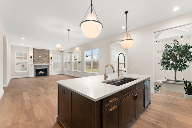 kitchen featuring a center island with sink, a fireplace, sink, and decorative light fixtures