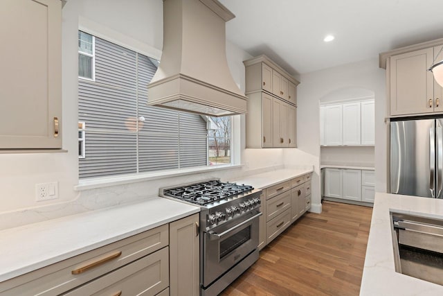 kitchen featuring hardwood / wood-style floors, custom exhaust hood, gray cabinets, light stone counters, and stainless steel appliances