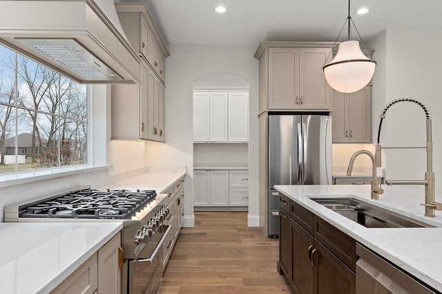 kitchen with appliances with stainless steel finishes, light wood-type flooring, light stone counters, custom exhaust hood, and pendant lighting