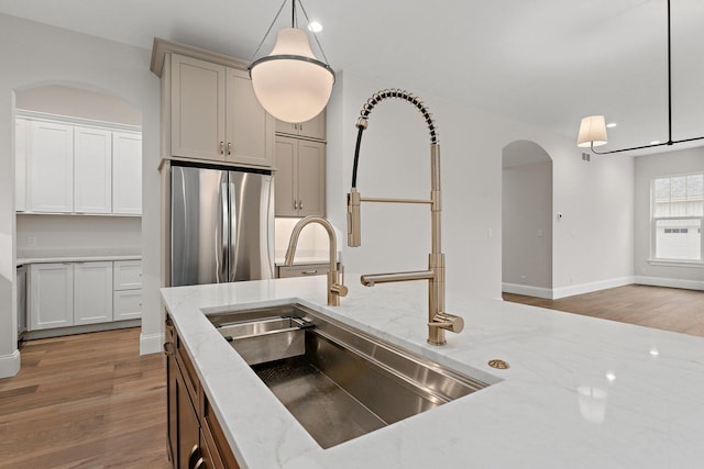 kitchen featuring stainless steel fridge, light stone counters, wood-type flooring, and hanging light fixtures