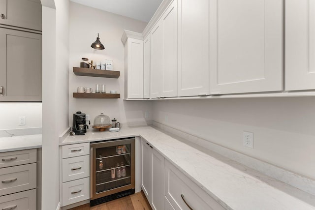 bar with white cabinetry, wine cooler, light stone counters, and light hardwood / wood-style flooring