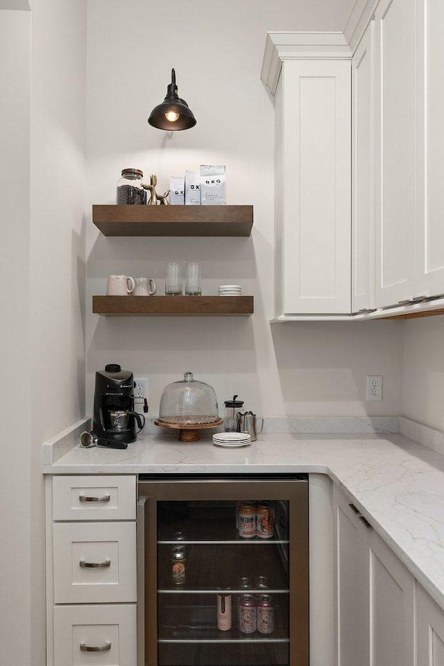 bar with wine cooler, white cabinetry, and light stone counters