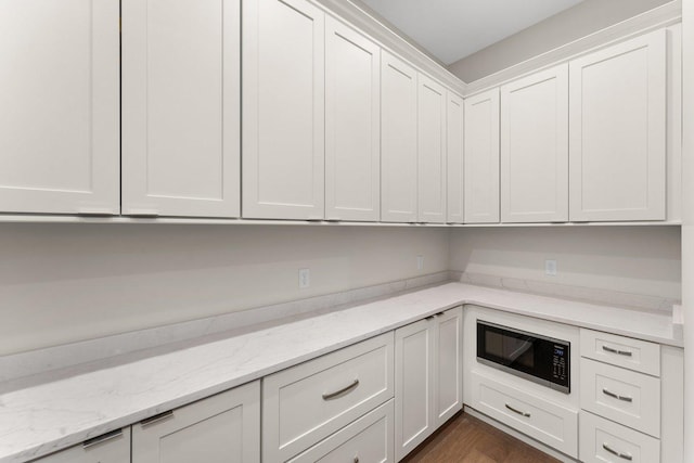 kitchen with black microwave, dark hardwood / wood-style flooring, white cabinets, and light stone countertops