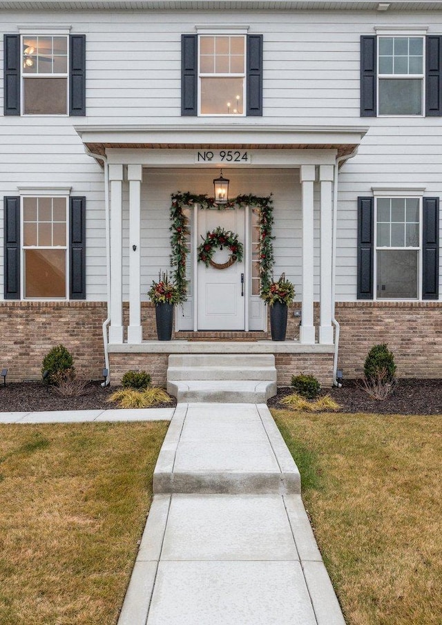 doorway to property featuring covered porch and a lawn