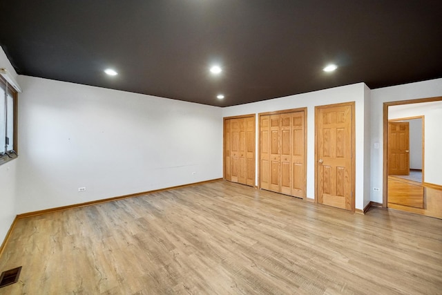 unfurnished bedroom with multiple closets and light hardwood / wood-style floors