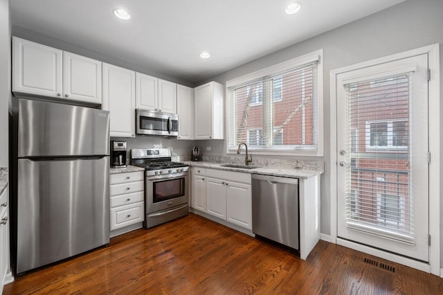 kitchen with dark wood-type flooring, white cabinets, sink, light stone countertops, and stainless steel appliances