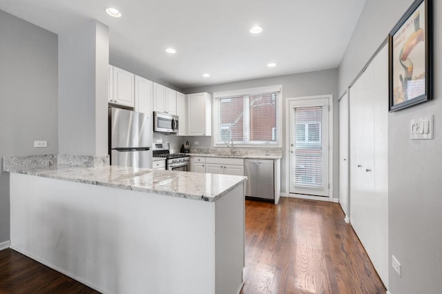 kitchen with kitchen peninsula, light stone countertops, stainless steel appliances, sink, and white cabinets