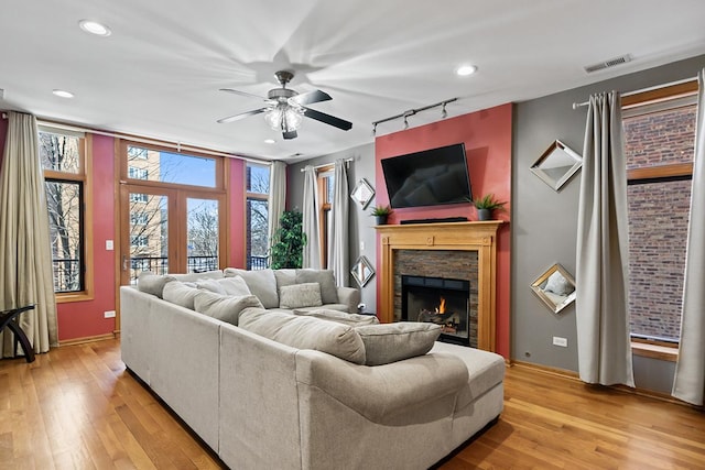 living room featuring ceiling fan, track lighting, light hardwood / wood-style flooring, and a stone fireplace