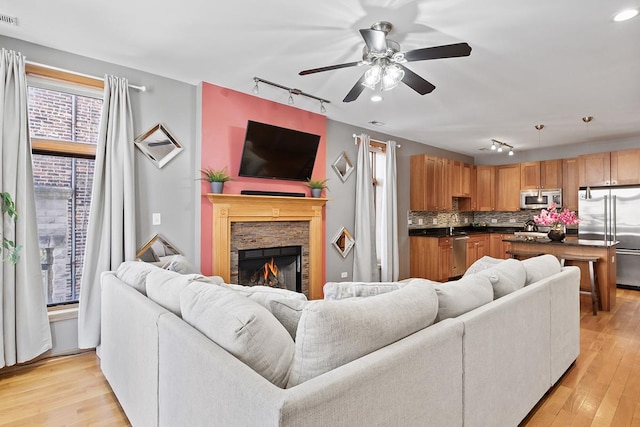 living room featuring ceiling fan, light wood-type flooring, a fireplace, and track lighting