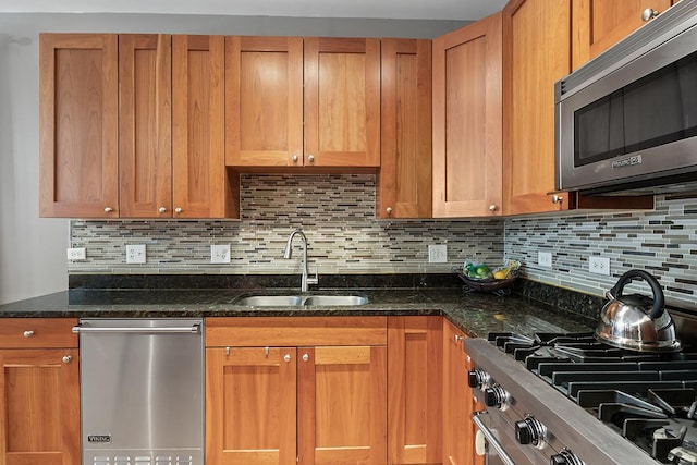 kitchen featuring stainless steel appliances, tasteful backsplash, dark stone counters, and sink