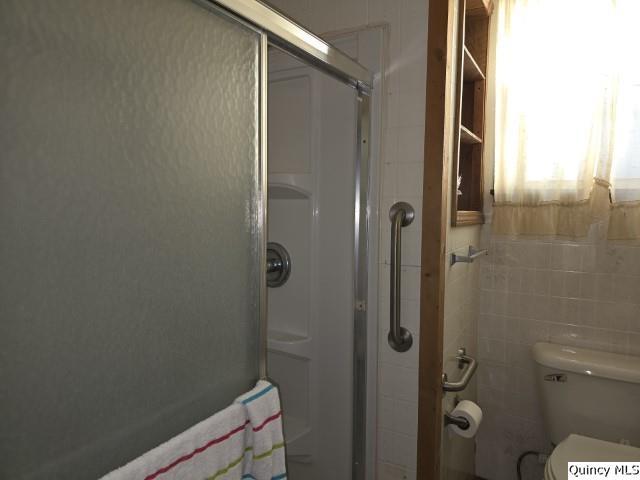 bathroom with tile walls, a shower with shower door, and toilet