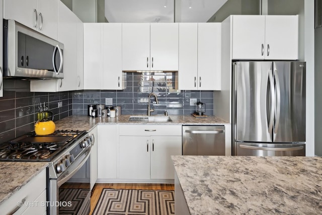 kitchen with stainless steel appliances, decorative backsplash, white cabinetry, a sink, and light stone countertops