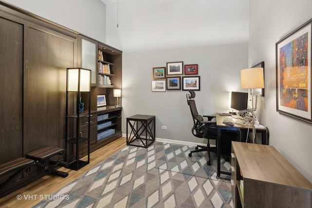 office space with light wood-style flooring, a high ceiling, and baseboards