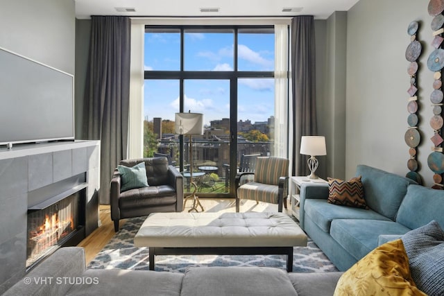 living room with wood finished floors, a wall of windows, a tile fireplace, and visible vents