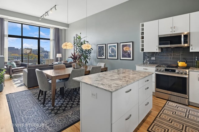 kitchen featuring light wood-type flooring, appliances with stainless steel finishes, decorative backsplash, and a center island