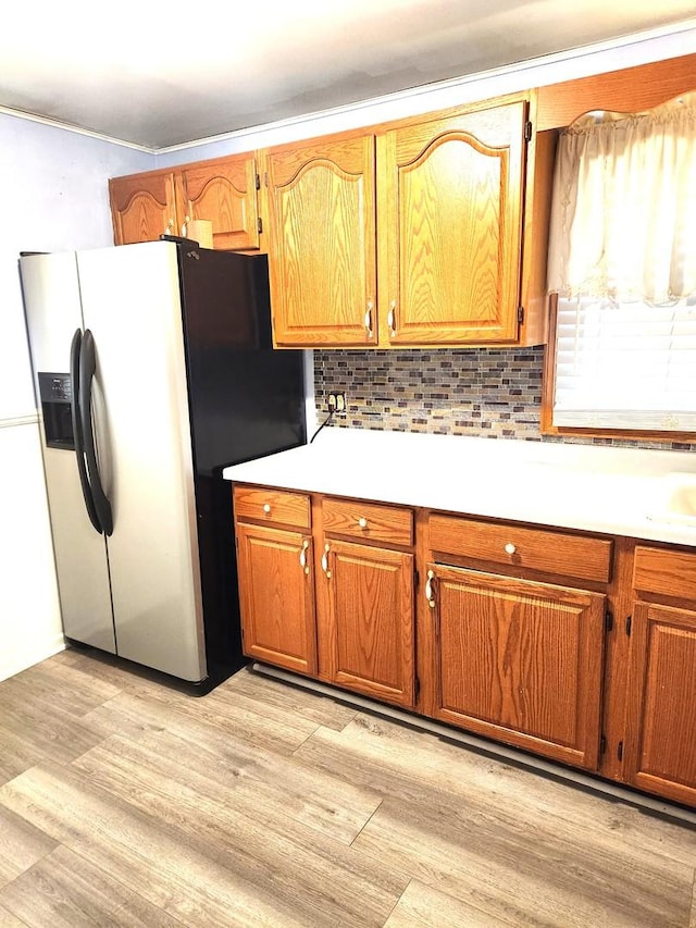 kitchen with brown cabinets, light countertops, light wood-style flooring, decorative backsplash, and stainless steel fridge