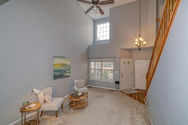 living area featuring carpet floors, a towering ceiling, and ceiling fan with notable chandelier