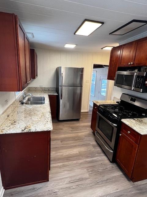 kitchen with light stone countertops, stainless steel appliances, light hardwood / wood-style floors, and sink