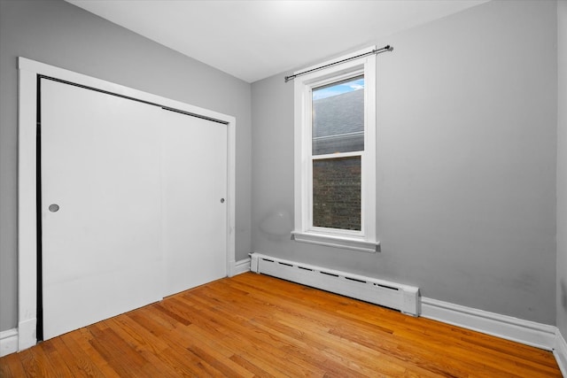 unfurnished bedroom featuring baseboard heating, a closet, and light wood-type flooring