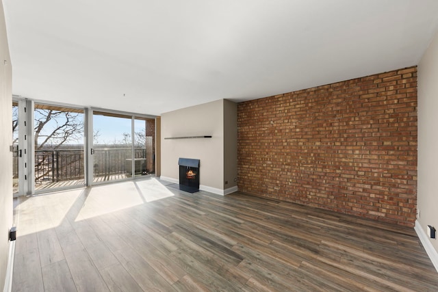 unfurnished living room with dark hardwood / wood-style flooring, expansive windows, and brick wall