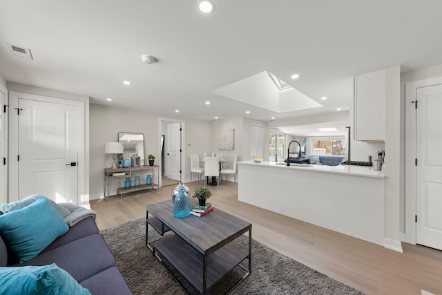 living room with light wood-type flooring, a skylight, and sink