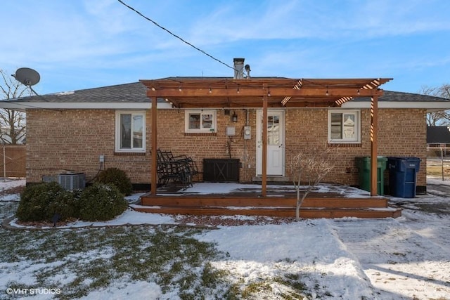 snow covered rear of property with cooling unit, a deck, and a pergola