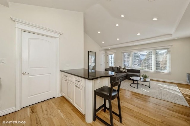 kitchen with vaulted ceiling, light wood-type flooring, a kitchen breakfast bar, kitchen peninsula, and white cabinets