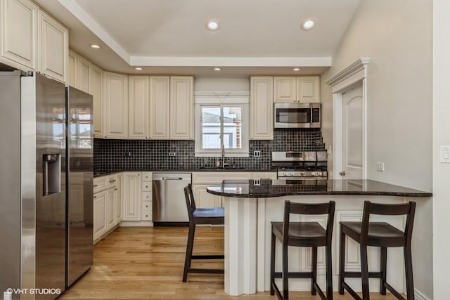 kitchen featuring sink, dark stone countertops, a kitchen bar, kitchen peninsula, and stainless steel appliances