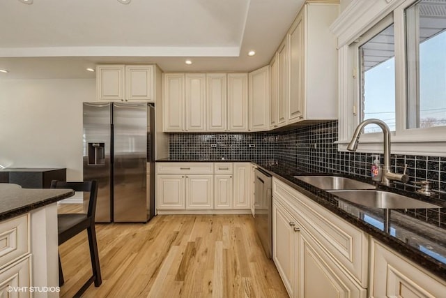 kitchen with sink, light hardwood / wood-style flooring, dark stone counters, stainless steel appliances, and backsplash