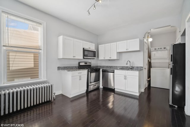 kitchen with white cabinets, radiator heating unit, stainless steel appliances, and stacked washer and clothes dryer