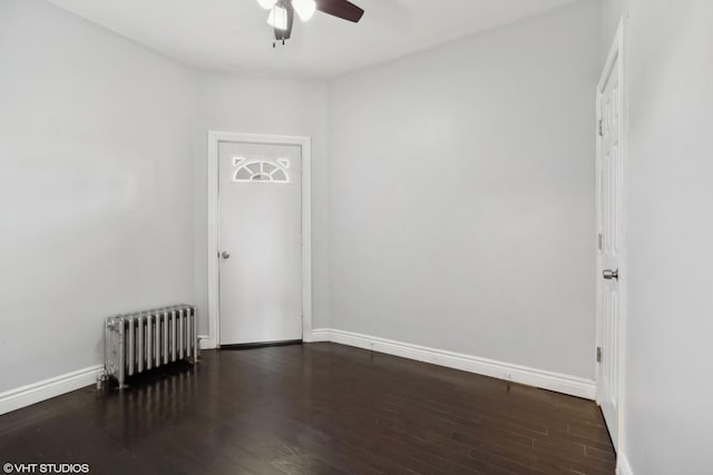 empty room featuring dark hardwood / wood-style flooring, radiator, and ceiling fan