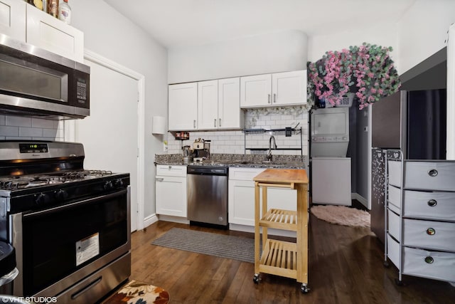 kitchen featuring white cabinets, stainless steel appliances, tasteful backsplash, and stacked washer / dryer