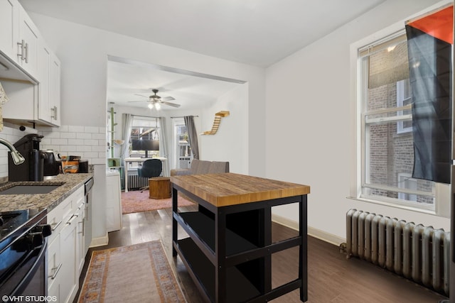 kitchen with dark stone counters, ceiling fan, sink, white cabinets, and radiator heating unit