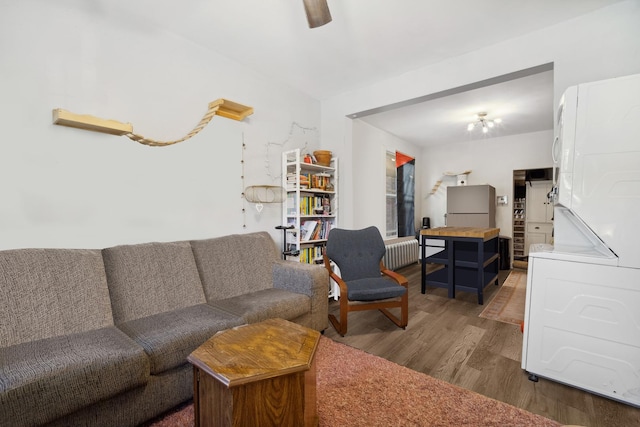 living room featuring hardwood / wood-style flooring, ceiling fan, radiator heating unit, and stacked washer and clothes dryer