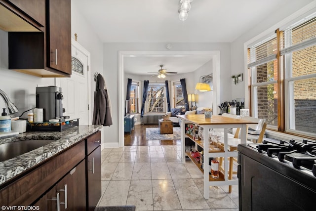 kitchen with sink, radiator heating unit, ceiling fan, light stone countertops, and dark brown cabinetry