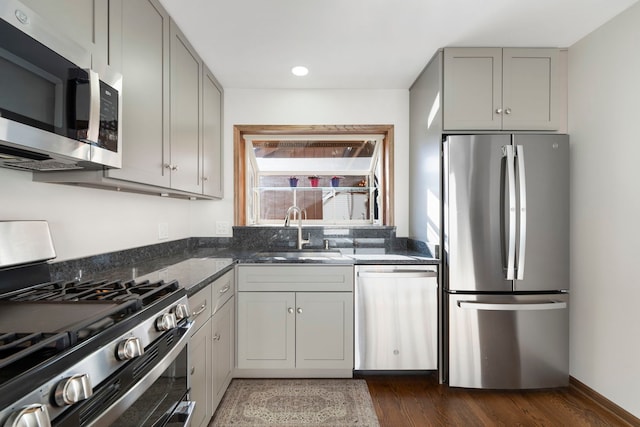 kitchen featuring sink, dark stone counters, dark hardwood / wood-style floors, gray cabinets, and stainless steel appliances