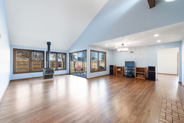 unfurnished living room featuring hardwood / wood-style flooring, a chandelier, high vaulted ceiling, and a wood stove