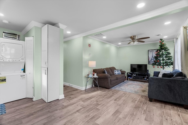 living room featuring stacked washing maching and dryer, ceiling fan, crown molding, and light hardwood / wood-style floors