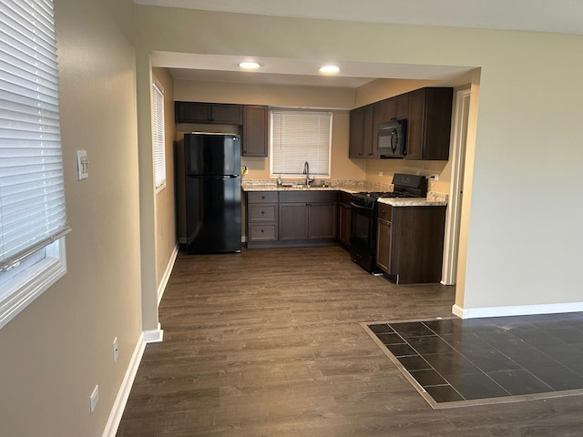 kitchen featuring black appliances, sink, light stone countertops, dark hardwood / wood-style flooring, and dark brown cabinetry