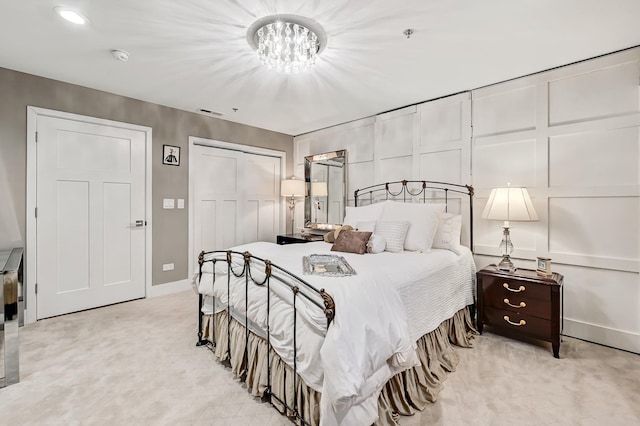 bedroom featuring a notable chandelier, a closet, a decorative wall, baseboards, and light colored carpet