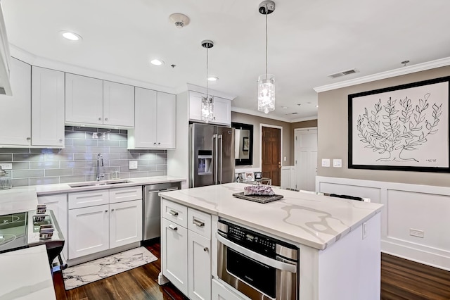 kitchen with appliances with stainless steel finishes, light stone counters, sink, white cabinets, and hanging light fixtures