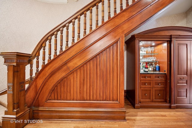 staircase featuring a bar, a textured wall, and wood finished floors