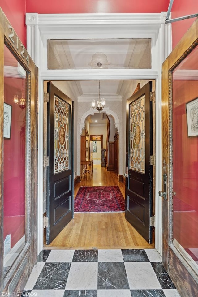 foyer entrance with arched walkways, ornamental molding, wood finished floors, and an inviting chandelier