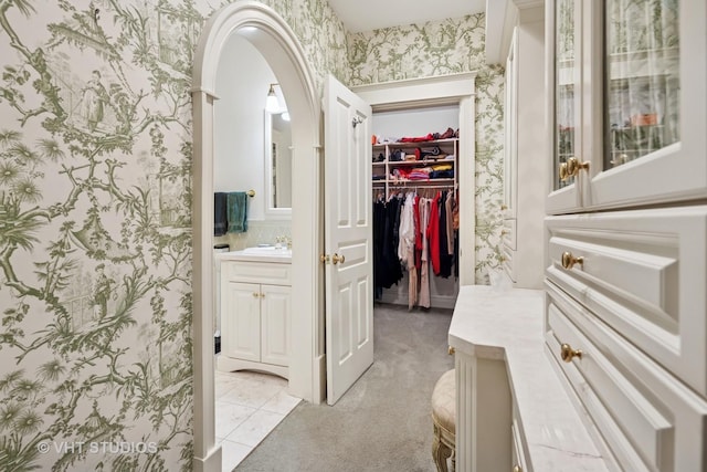 bathroom with a spacious closet, wallpapered walls, and vanity