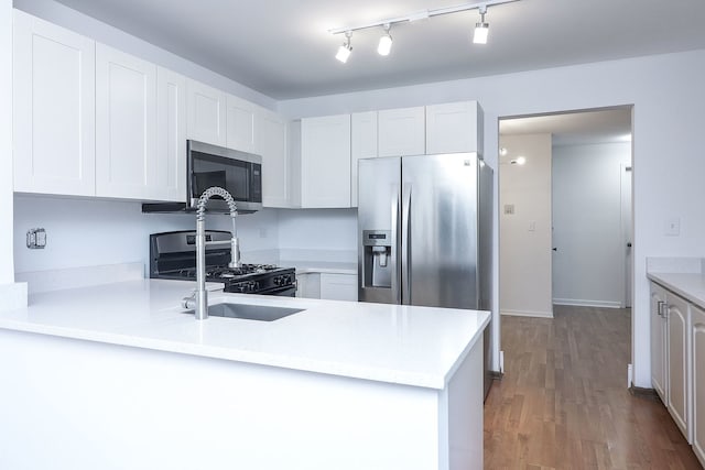 kitchen with kitchen peninsula, light hardwood / wood-style flooring, stainless steel appliances, white cabinets, and sink